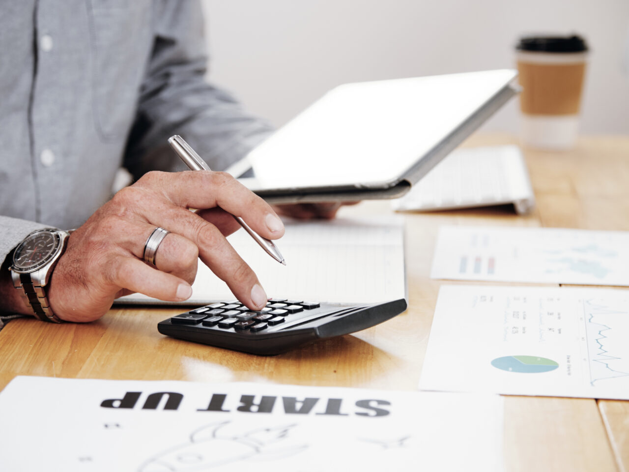 Close-up of businessman counting the profit of the company and using digital tablet at office desk